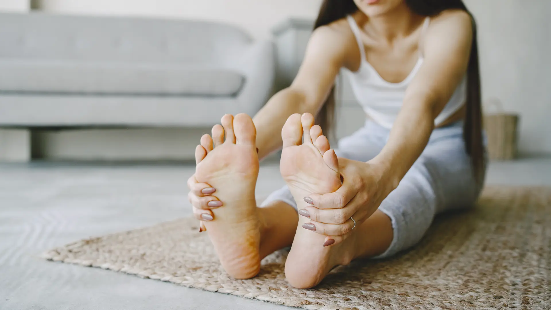 Mulher sentada no chão segurando os pés com as pernas esticadas 