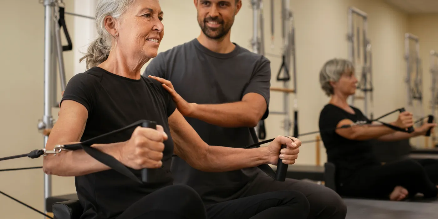 Senhora fazendo exercícios de pilates acompanhada por seu instrutor.