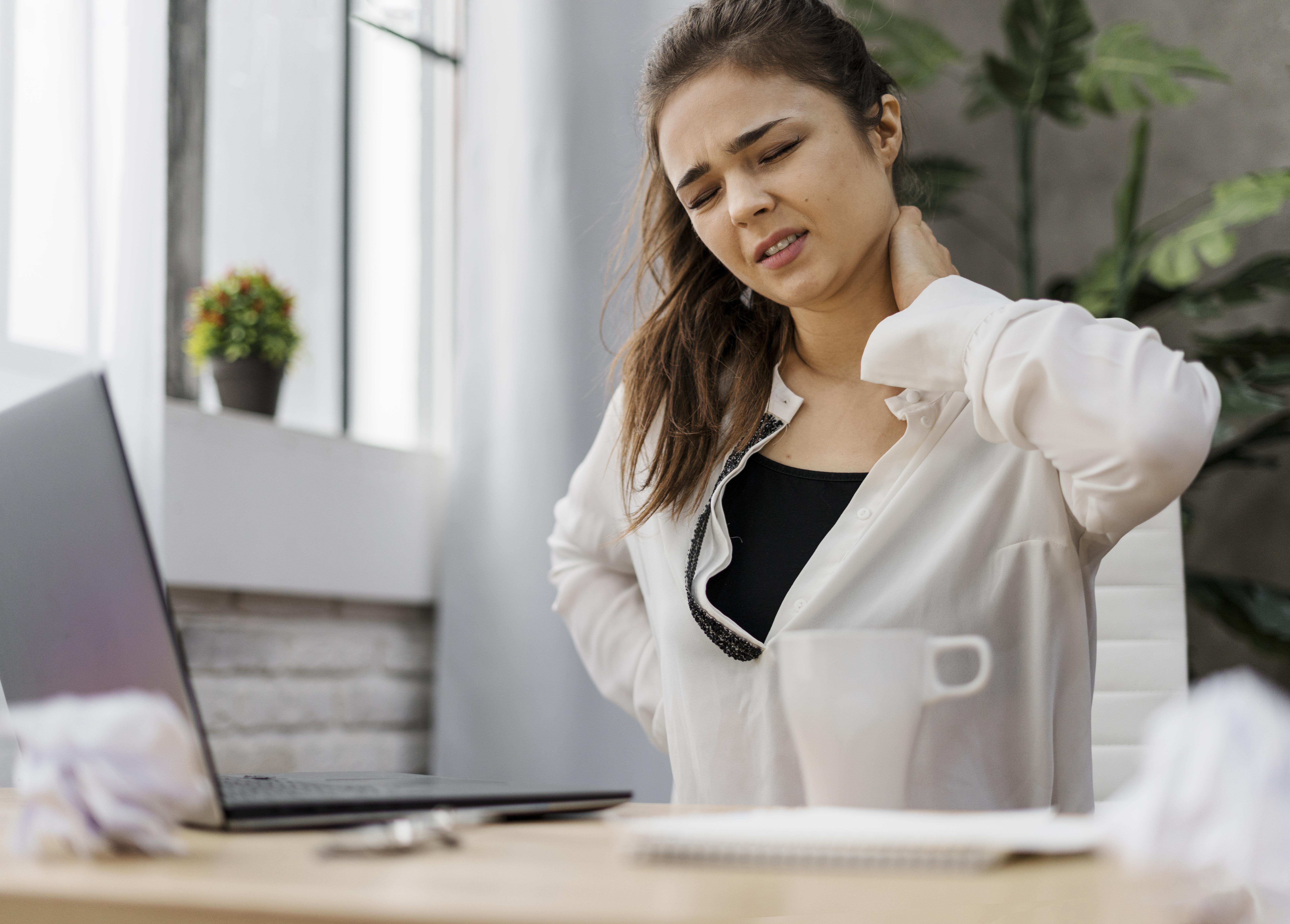 Mulher sentada em frente ao computador sentindo dor na coluna